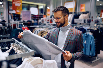 Happy man looking for shirt while shopping in clothing store at mall.