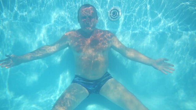 Elderly man sits on bottom of pure blue pool underwater