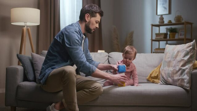 Father spending time with little daughter. Baby girl throwing colored cubes at floor. Father building tower of colored cubes. Man spending leisure playing with kiddo. Father clapping hands.