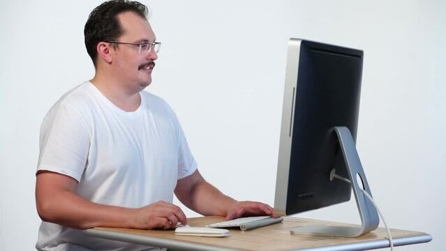 Man in white t-shirt looks at monitor of computer and laughs