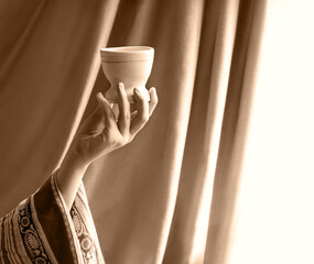 A hand in ancient clothing holds a clay bowl