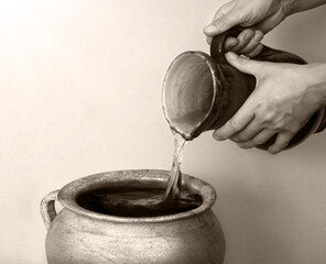 A hand holds a clay jar and pours water