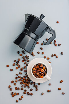 Bialetti moka pot. Coffee maker and coffee beans in mug on gray background. Top view.