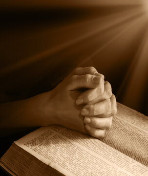 Hands clasped in prayer near an open book