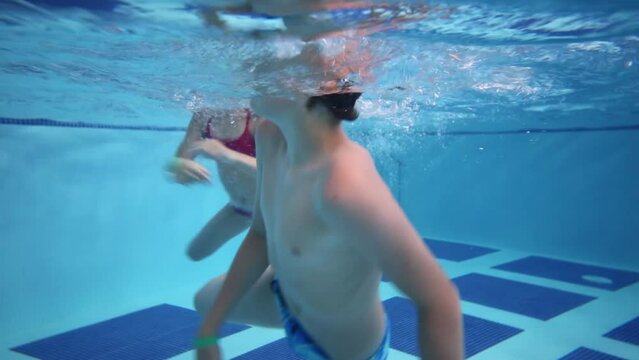 Boy and girl in goggles swim underwater in blue pool