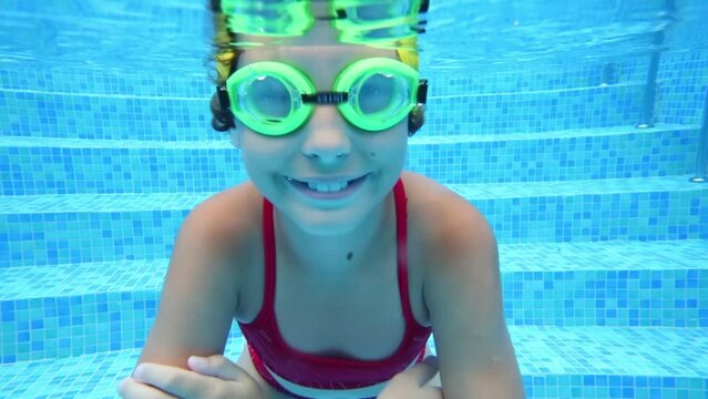  Happy girl in goggles swim underwater in pool. Close up
