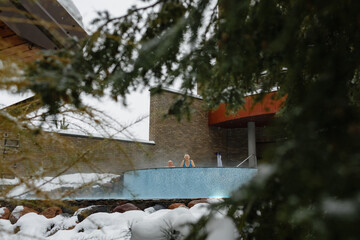 An elderly woman and a man relax together in a swimming pool with hydromassage outdoors in winter.