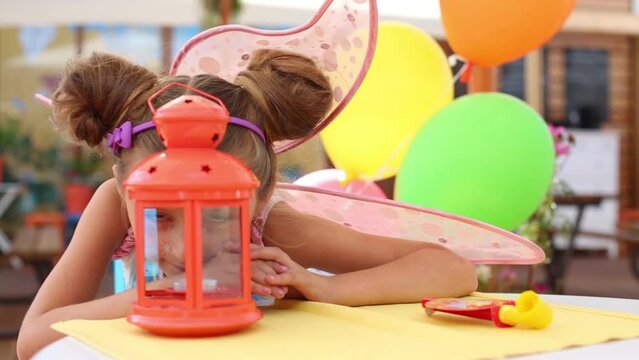 Girl in fairy costume in cafe hides behind lantern on table