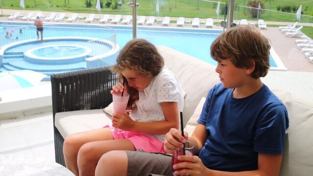 Boy and girl drink cocktails on sofa at terrace near pool