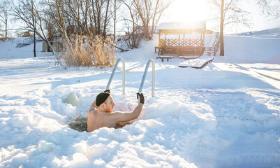 Young man enjoying winter swimming in a hand-cut ice hole on a sunny snowy day
