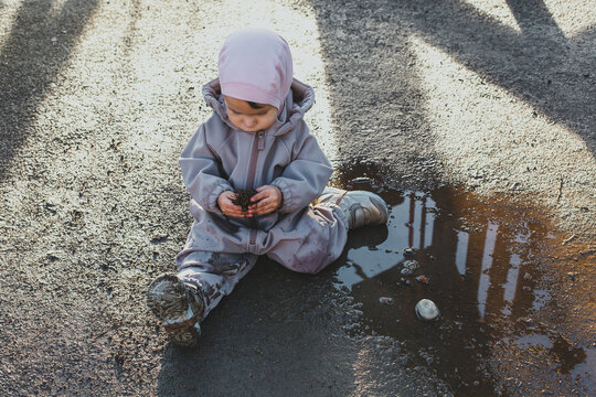 a child discovers the world, one small child in dirty clothes 1 year and 3 months old sits in a puddle and plays with a cone, the concept of childhood and walks