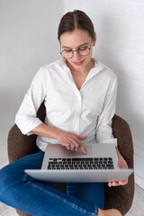Woman freelancer wearing white shirt and jeans doing her remote work on computer.