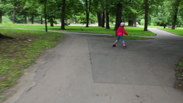 Back of girl in jeans roller-skates in summer green park