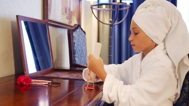 girl in robe and towel sit in front of mirror and holds paper