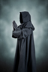 Medieval monk in hooded cloak praying in the dark
