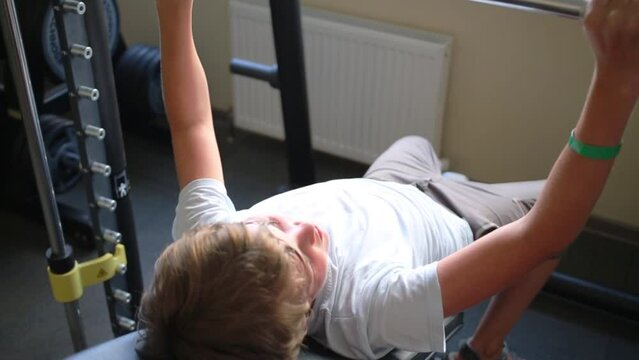 Boy teen raises barbell on exerciser in fitness center