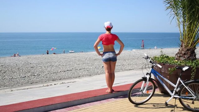 Back of woman in shorts looking at stony beach at summer