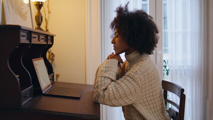 Serious woman work computer at vintage table. African freelancer typing laptop