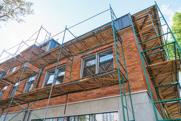 Scaffolding is installed along the wall of the building under construction. Plastering and painting...
