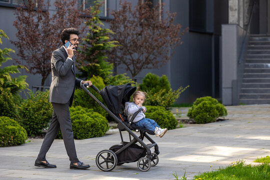 Elegant young man talking on the phone and carrying a baby carriage