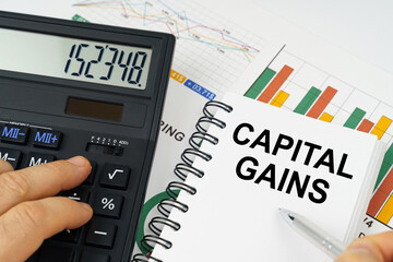 On the table there is a calculator, reports with graphs and a notepad with the inscription - Capital gains