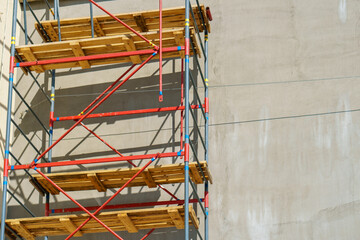 Scaffolding is installed along the wall of the building under construction. Plastering and painting of the facade of the house. Metal supports and wooden platforms for working at height.