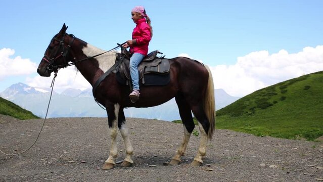 Happy girl learns to control of horse among mountains at summer