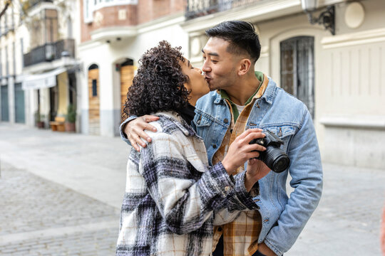 young multicultural people in love walk down the street kissing with their camera in hand
