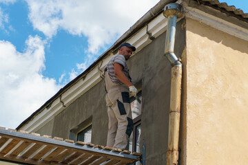 The builder works standing on a wooden scaffolding support. Painting and plastering of the walls of...