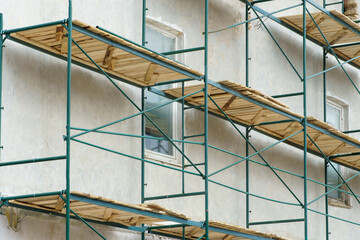 Scaffolding is installed along the wall of the building under construction. Plastering and painting of the facade of the house. Metal supports and wooden platforms for working at height.