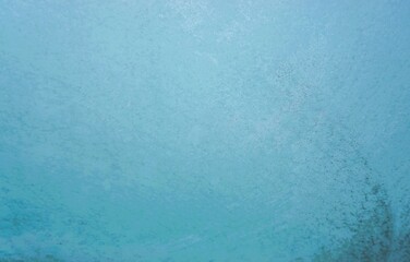 Eisbedeckte Glasscheibe mit Muster vor blauem Himmel bei Frost und Schnee am Morgen im Winter