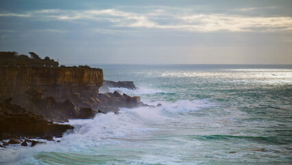 Ocean washing coastal cliffs on gloomy day. Stormy sea breaking rocks in evening