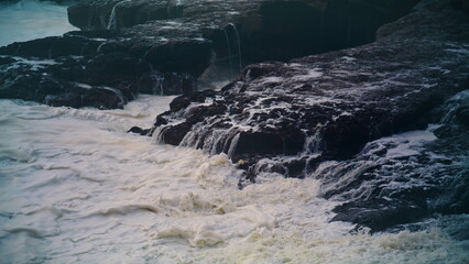 White ocean washing rocks on storm day. Closeup foaming waves hitting coastline