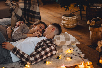 Beautiful young loving couple relaxing near fireplace in bed at home. Happy spouses enjoying lazy...