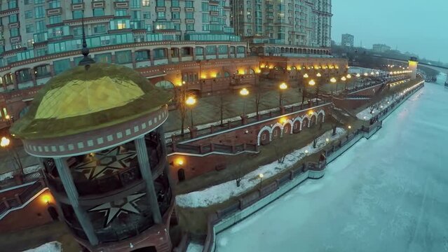 Rotunda on quay near dwelling house and icy river at winter