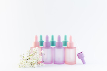 Set of colorful cosmetic bottles with dropper and beautiful flowes on white background close up.=, copy space for your design. Spring cosmetic sale and promo banner.