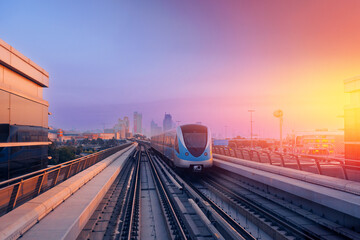 Dubai cityscape, modern metro railway with skyscrapers, sunset. Traffic train and building with urban skyline background of city UAE