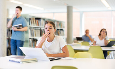 Fototapeta premium View on bored young caucasian latina student with a laptop in the school library