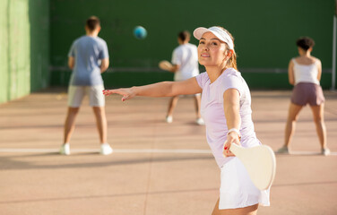 Sporty young Argentinian woman playing traditional team match of pelota at open-air fronton on...