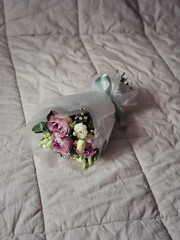 Vertical close up of a bouquet of purple and white roses, eucalyptus and white gypsophila on a bed with pastel blanket.