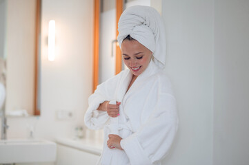Smiling happy young woman in white robe and a towel on her head