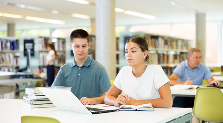 Obraz premium Friendly young woman offering assistance to male friend studying, finding information at university library