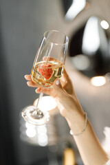 Close-up of young woman's hand holding glass of champagne with strawberries