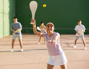 Portrait of sporty young girl playing paleta fronton on outdoor court, ready to hit ball. Healthy and active lifestyle concept