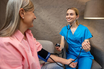 Nurse or doctor checking blood pressure to senior woman.