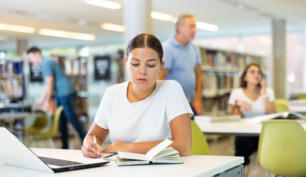 Caucasian school student girl doing research on project laptop in the college library