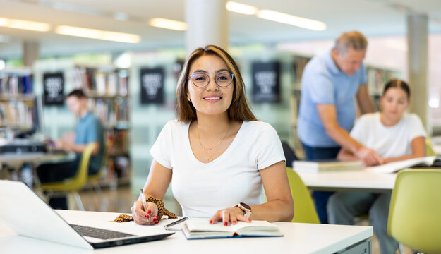 Portrait of adult latino woman studying at library using books and laptop computer