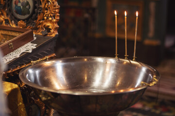 Metal basin (font) with three candles for bathing babies during the baptismal ceremony in the temple. christening in the monastery. Ceremony of a christening in Christian church. baptismal font flower - obrazy, fototapety, plakaty