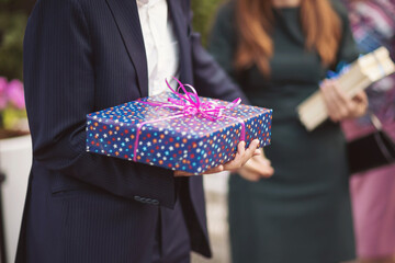 Male hand holding ornate gift box. Man holding a white gift box wrapped with pink ribbon.