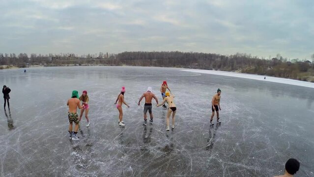 Young people in underwear slide on skates by icy pond at winter